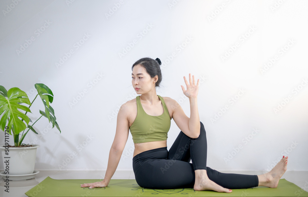Fototapeta premium Woman doing yoga on the green yoga mat to meditate and exercise in the home.