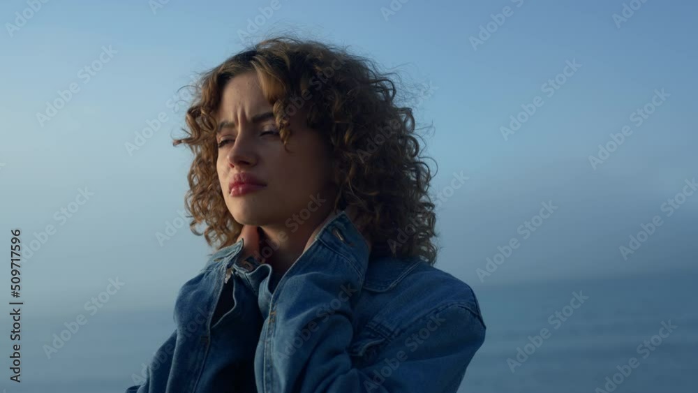 Sad girl standing on ocean beach. Distressed woman touching neck with hands Sad girl standing on ocean beach. Distressed woman touching neck with hands