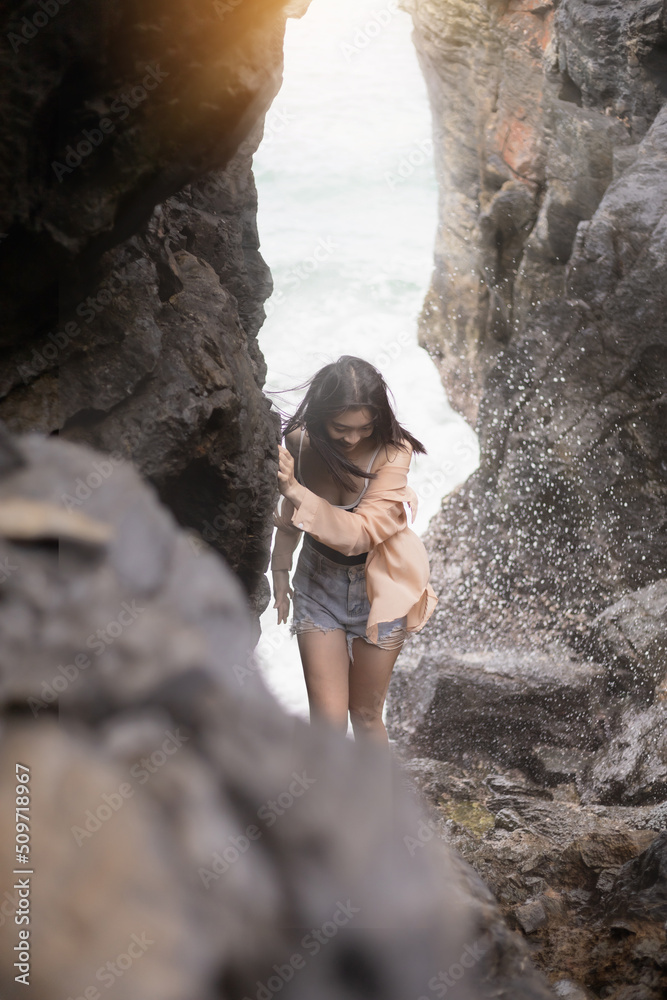 A young woman is scrambling to escape the sea waves splashing from a cave on the beach.