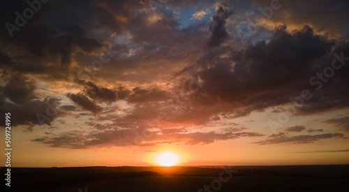 Bright colorful sunset sky with setting sun and vibrant clouds over dark landscape