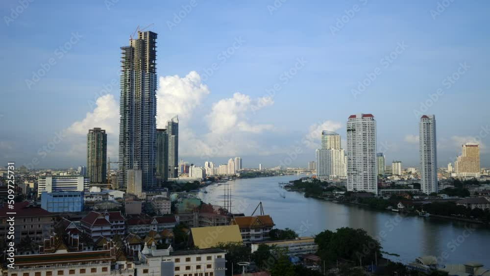 Cityscape in shadow from clouds, cumulus congestus formation towering on back. Time lapse view of Bangkok in day. Boats rush forth and back along Chao Phraya rivers, tall buildings along riverbanks Cityscape in shadow from clouds, cumulus congestus formation towering on back. Time lapse view of Bangkok in day. Boats rush forth and back along Chao Phraya rivers, tall buildings along riverbanks