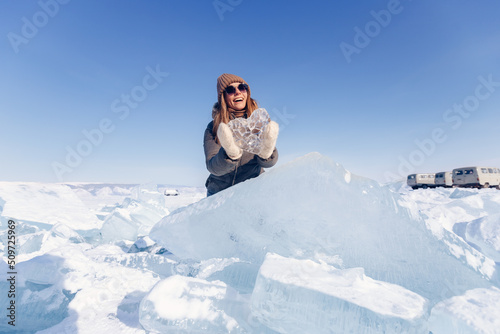 Happy tourist in sunglasses holds crystal clear ice on background of winter lake Baikal