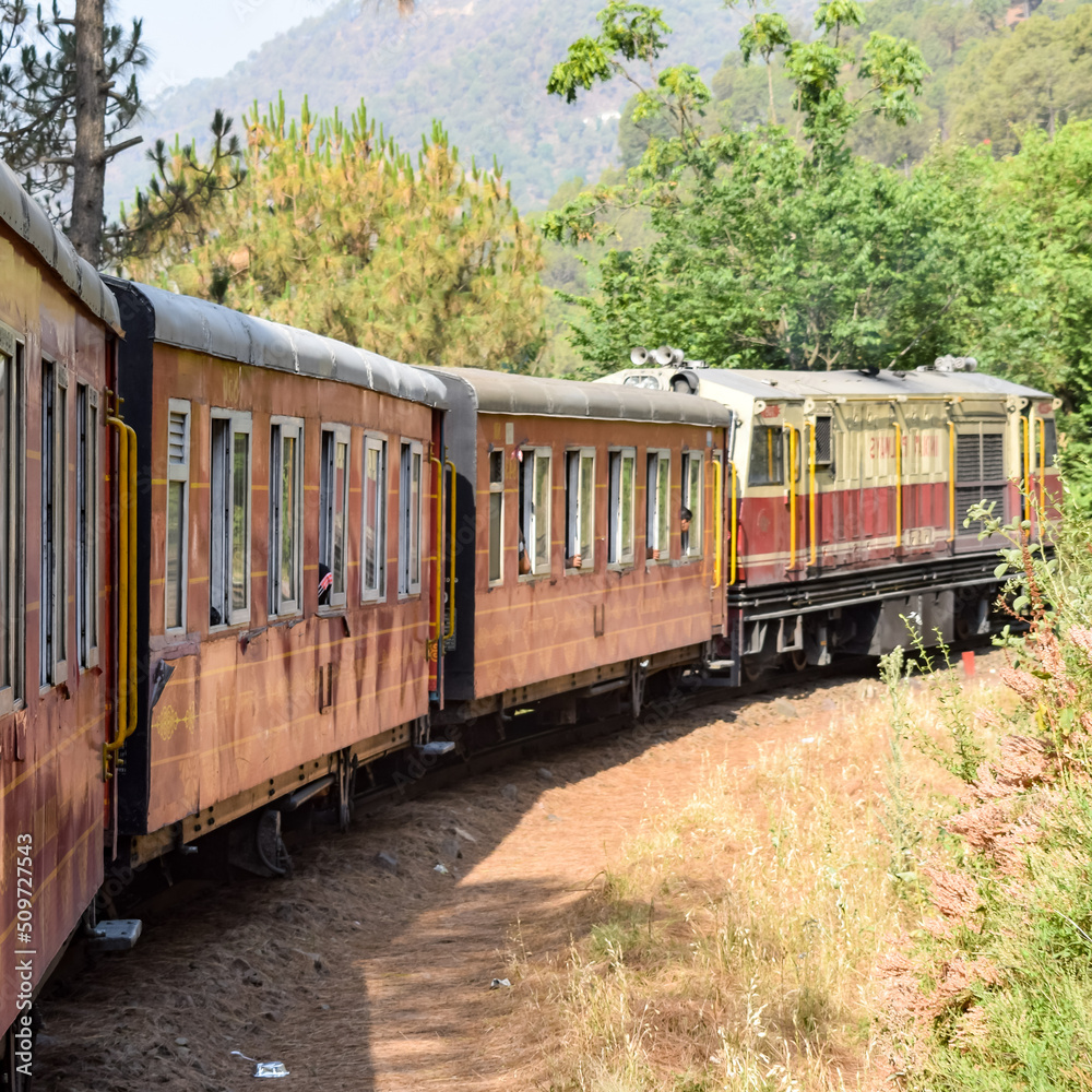 Toy Train moving on mountain slopes, beautiful view, one side mountain, one side valley moving on railway to the hill, among green natural forest. Toy train from Kalka to Shimla in India