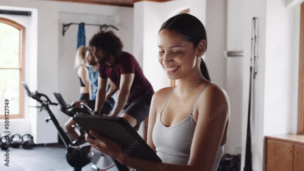 Happy and proud young adult biracial female gym owner using technology to run indoor fitness gym. Busy fitness class.