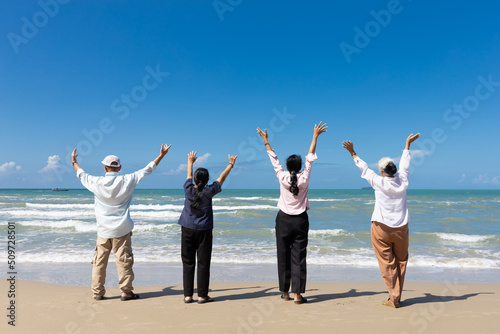 portrait back view group of seniors man and women with arms raised on the beach
