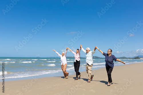 group of seniors man and women walking and arms raised together on the beach