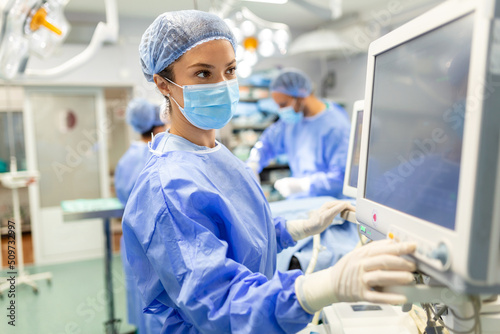 Anesthetist Working In Operating Theatre Wearing Protecive Gear checking monitors while sedating patient before surgical procedure in hospital