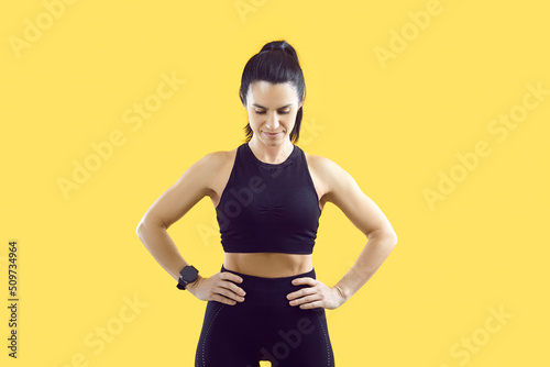 Wallpaper Mural Confident sportswoman holding hands on waist standing in workout pose on vivid yellow background. Woman with fit body in black sportsbra, leggings and with smart watch performs physical exercises. Torontodigital.ca