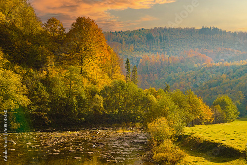 Fototapeta Naklejka Na Ścianę i Meble -  View of the river idyllic landscape when the sun is about to set over the hill on a colorful autumn day.