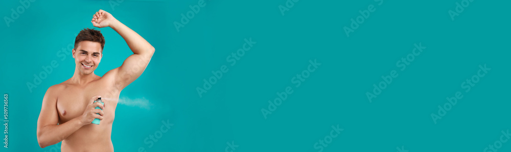 Young man applying spray deodorant to armpit on turquoise background, space for text. Banner design Young man applying spray deodorant to armpit on turquoise background, space for text. Banner design