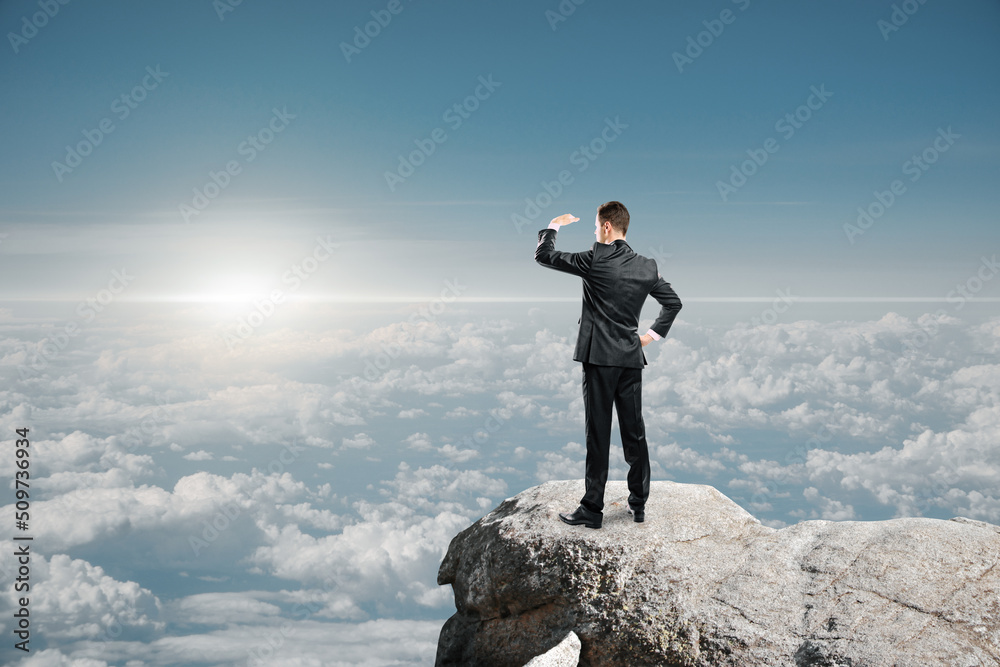 businessman standing on cliff and looking into the distance on bright blue sky and clouds background with mock up place for your advertisement. Market research, exploration and future concept. businessman standing on cliff and looking into the distance on bright blue sky and clouds background with mock up place for your advertisement. Market research, exploration and future concept.
