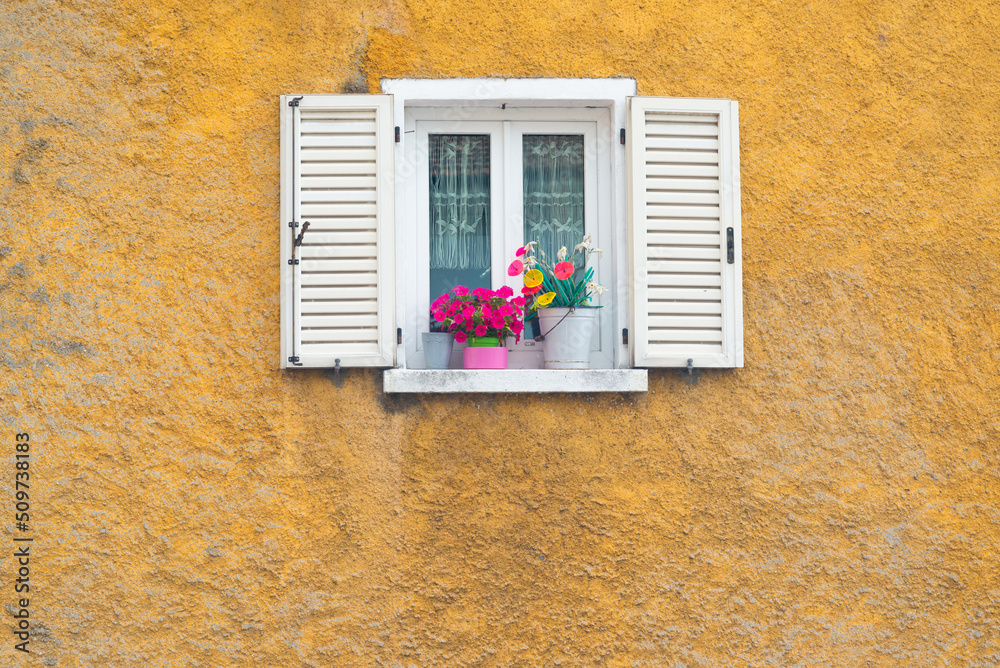 White wooden window opened on a yellow wall with colorful flowers in the ancient village named 