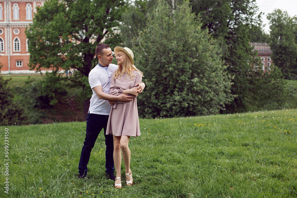 Fototapeta premium man and a woman in love in a dress and hat are stand on a green field under a tree in summer.