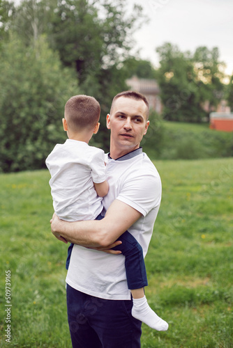 father embraces son standing on a field with grass in summer.