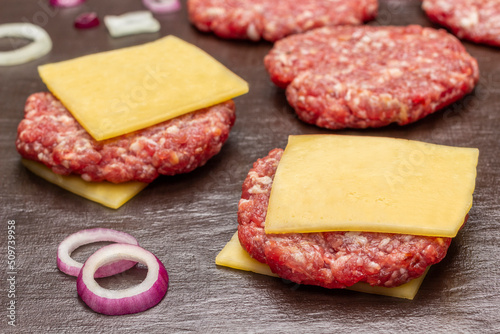 Raw beef burgers with cheese on brown background.
