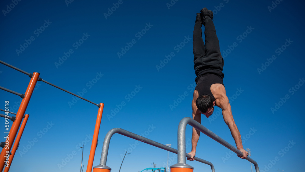Shirtless man doing handstand on parallel bars at sports ground. 