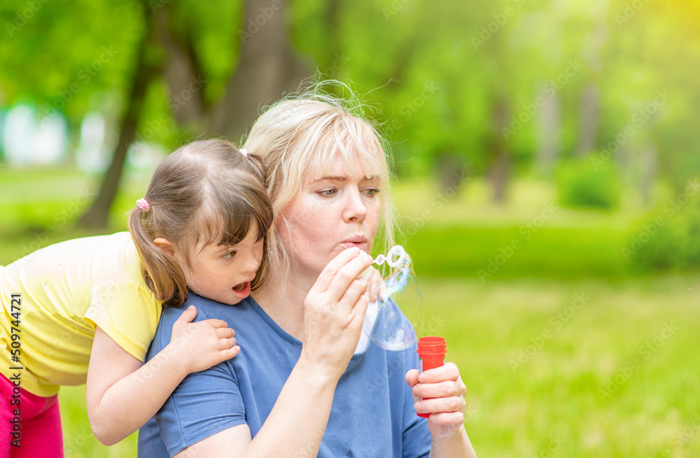 Woman and little girl with Downs syndrome blow bubbles at summer park Woman and little girl with Downs syndrome blow bubbles at summer park