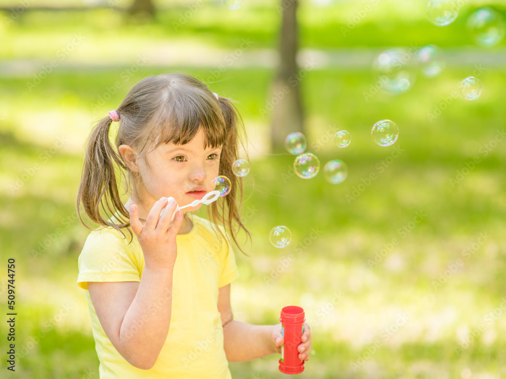 Little girl with Downs syndrome blows soap bubbles at summer park Little girl with Downs syndrome blows soap bubbles at summer park