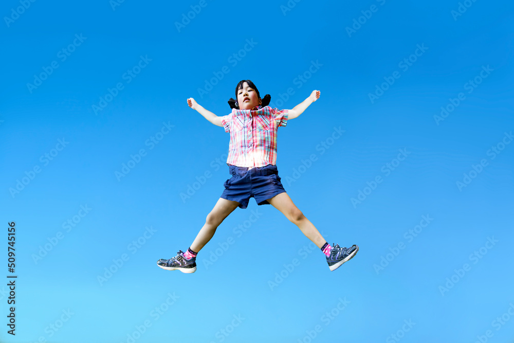 青空を背景に手足を広げジャンプする幼い女の子1人