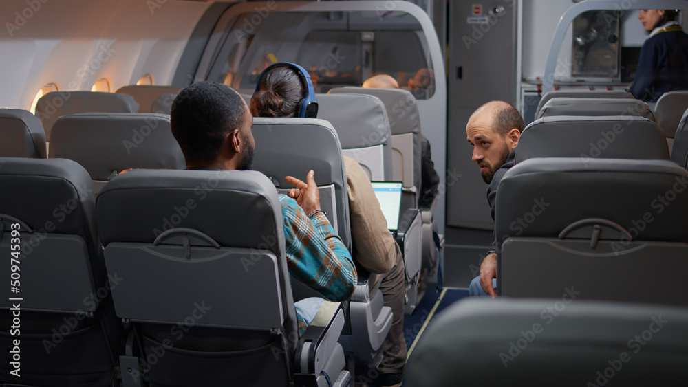 Diverse travellers having conversation in airplane before takeoff, flying with international airline to go on holiday vacation. Travelling by plane with flight attendant, commercial airways. Diverse travellers having conversation in airplane before takeoff, flying with international airline to go on holiday vacation. Travelling by plane with flight attendant, commercial airways.