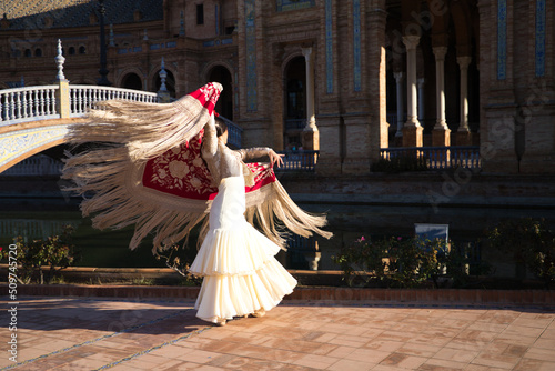 Flamenco dancer, woman, brunette and beautiful typical spanish dancer is dancing with a red manila shawl in a square in seville. Flamenco concept of cultural heritage of humanity.