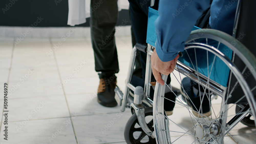 Obraz premium Senior patient with chronic disability using wheelchair in waiting room at hospital reception area to meet with doctor for appointment. Man with health condition doing checkup visit. Close up.