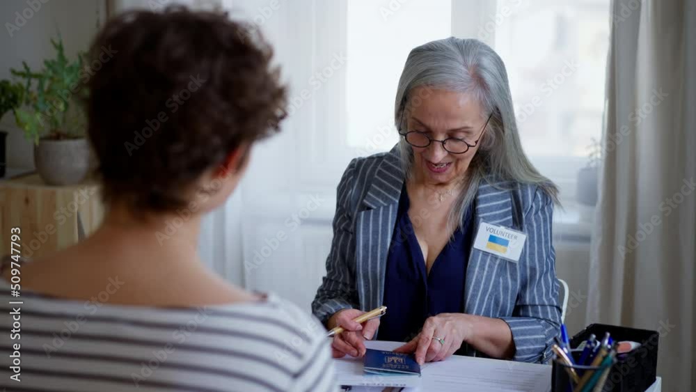 Senior woman volunteer helping Ukrainian woman to fill in forms at asylum centre. Senior woman volunteer helping Ukrainian woman to fill in forms at asylum centre.