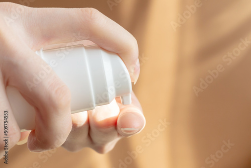 Mockup of packaging for cosmetic products. Women's hands squeeze foam for washing from bottle with dispenser onto finger. Close-up, brown background. Concept of body care, hand disinfection