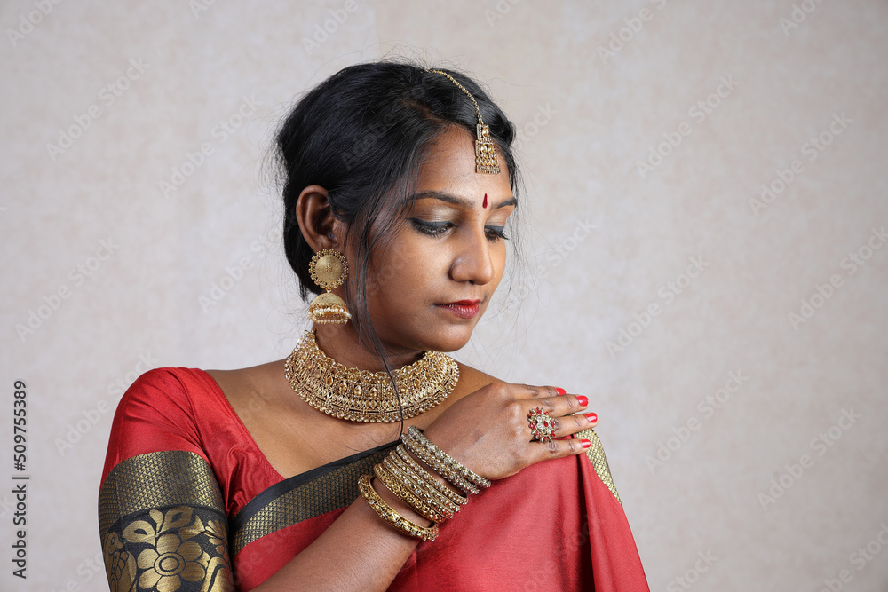 Indian woman wearing red orange traditional royal saree jewellery choker  set necklace jhumka earring maang tikka waist chain stand pose look see  smile mood expression at old rustic room background Stock Photo