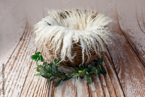 brown wicker basket for a newborn photo shoot on a wooden background. props for a photo shoot, decorated with olive branches. sheep wool rug