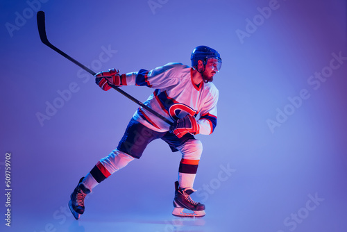 In action. Professional hockey player in sports uniform and protective equipment skating isolated on purple background. Concept of sport  active lifestyle  motion  movement  ad.