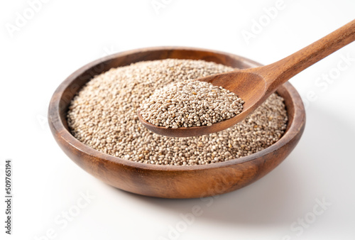White chia seeds in a wooden dish set against a white background and scooped up with a spoon.