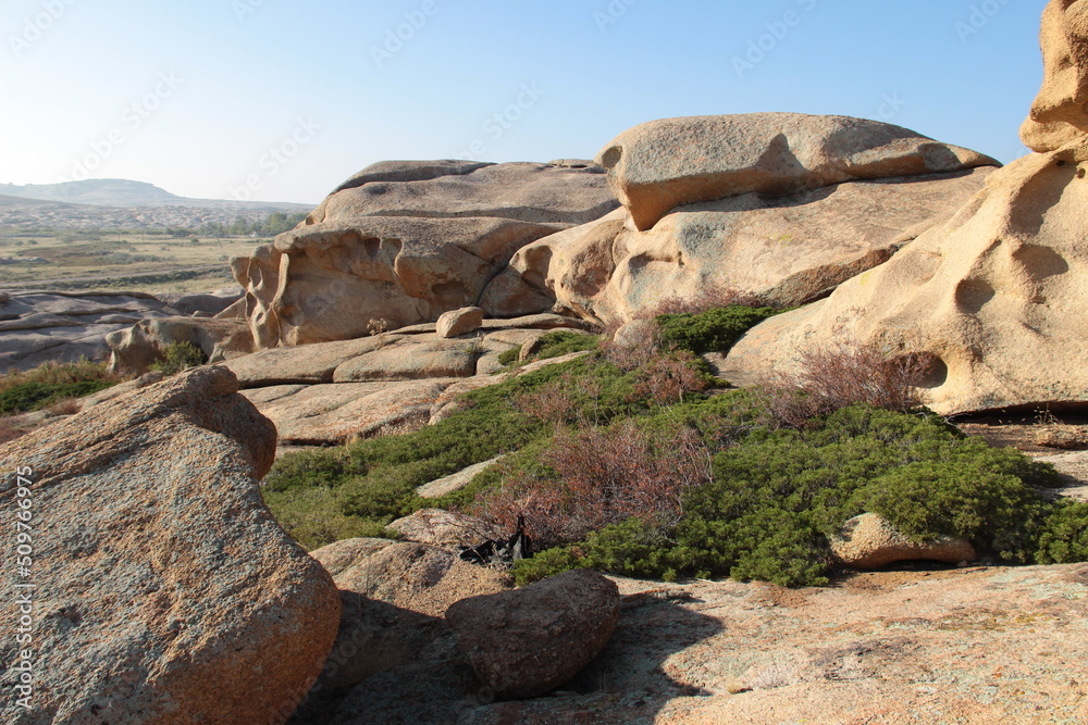Smooth large volcanic rocks in the Bektau-Ata tract overlooking the valley, green bushes on the rocks, clear sky, summer, sunny Smooth large volcanic rocks in the Bektau-Ata tract overlooking the valley, green bushes on the rocks, clear sky, summer, sunny