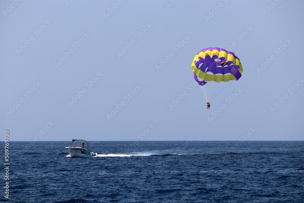 Parasailing on the sea, speed boat and couple on parachute in blue sky. Beach vacation, extreme water sports Parasailing on the sea, speed boat and couple on parachute in blue sky. Beach vacation, extreme water sports
