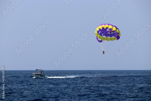 Parasailing on the sea, speed boat and couple on parachute in blue sky. Beach vacation, extreme water sports