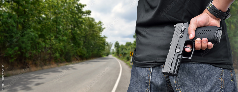 Robber holds 9mm automatic pistol gun in right hand and stands beside the road in countryside to robber the  passengers and drivers who passing this road, robbery on the road concept.