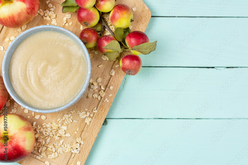 Φωτογραφία Oatmeal porridge for the baby from ground cereals in a blue bowl, red ripe apples on a wooden board on a blue background