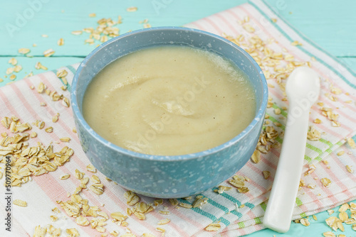 Oatmeal porridge for the baby from ground cereals in a blue bowl, a spoon on a mint wooden background. Baby's first complementary food, baby nutrition.