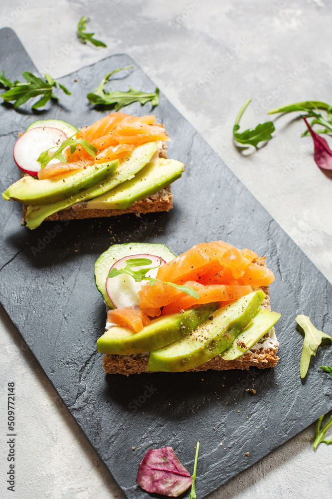 Two open sanwiches with dark rye bread, avocado, smoked salmon and radish
