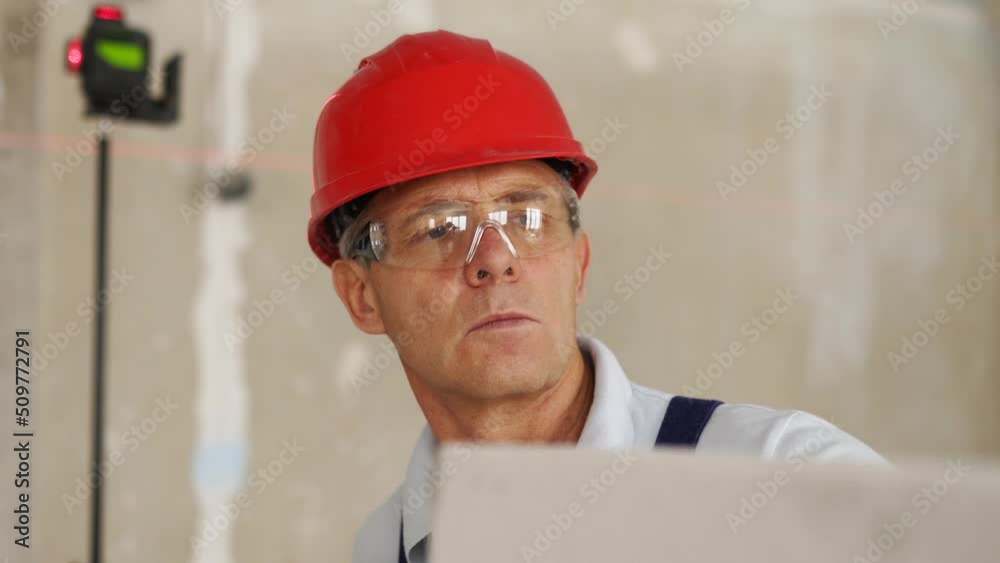 Bricklayer using rubber mallet hammer to tap and level concrete blocks wall. Contractor uses precise spirit bubble and laser level for brickwork. Worker constructs a wall in new apartment real estate. Bricklayer using rubber mallet hammer to tap and level concrete blocks wall. Contractor uses precise spirit bubble and laser level for brickwork. Worker constructs a wall in new apartment real estate.