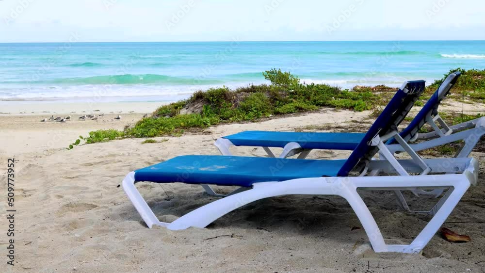 The beautiful beach front of the Cuban beach at Varadero in Cuba showing the waves and clean ocean waters with two deck chairs on the sandy beach filmed in 8k quality The beautiful beach front of the Cuban beach at Varadero in Cuba showing the waves and clean ocean waters with two deck chairs on the sandy beach filmed in 8k quality