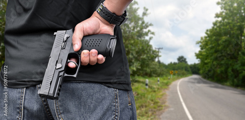 Robber holds 9mm automatic pistol gun in right hand and stands beside the road in countryside to robber the passengers and drivers who passing this road, robbery on the road concept.