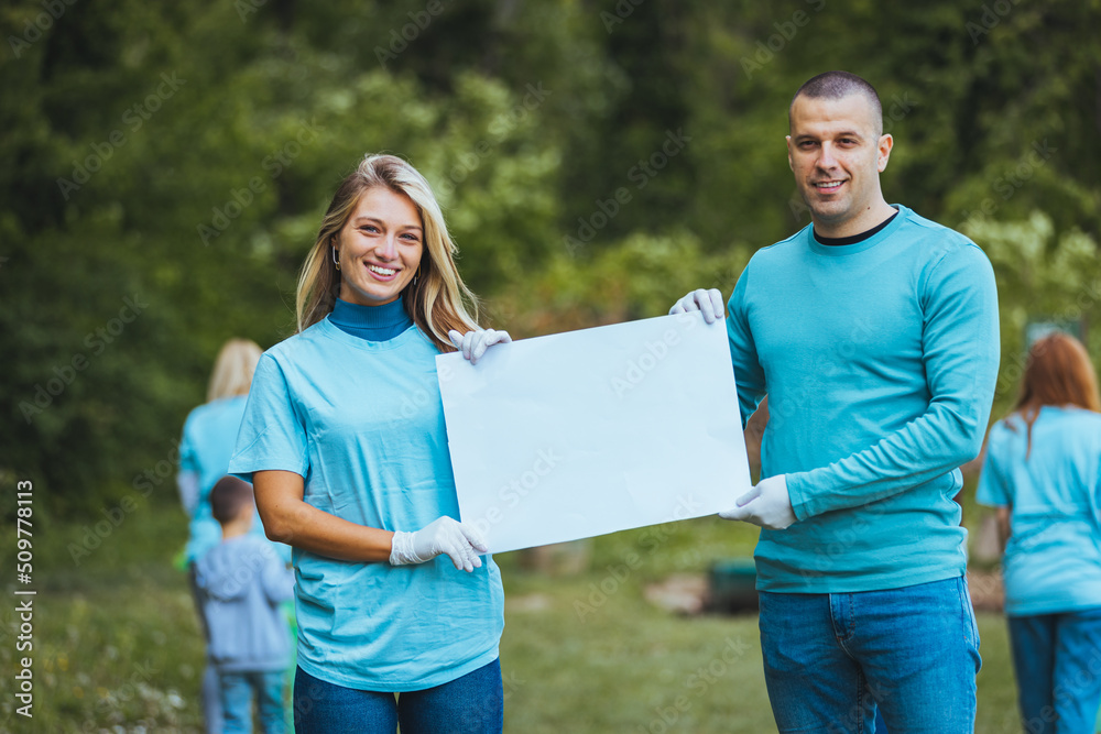 Naklejka premium A couple holding a poster in their hands and showing it to the camera, posing standing in nature, smiling at the camera.