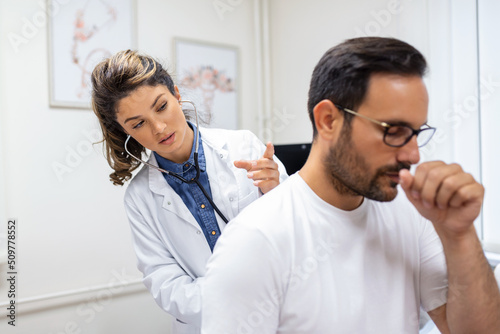 A female doctor at the clinic performs auscultation of the lungs of a patient with symptoms of coronavirus or pneumonia. He is coughing the doctor listens to the wheezing in the lungs photo