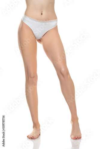Front view of female barefoot legs in white bikini panties on a white studio background