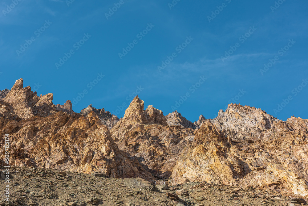 Scenic mountain landscape with sharp rocks under blue sky in sunny day. Colorful scenery with gold sunlit sharp rocky mountains. Sharp rocks in bright sun. High rocky mountains in golden sunlight. Scenic mountain landscape with sharp rocks under blue sky in sunny day. Colorful scenery with gold sunlit sharp rocky mountains. Sharp rocks in bright sun. High rocky mountains in golden sunlight.