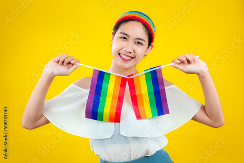 Happy asian woman holding pride flag rainbow isolated yellow color background. lgbtq and lgbtq+ concept