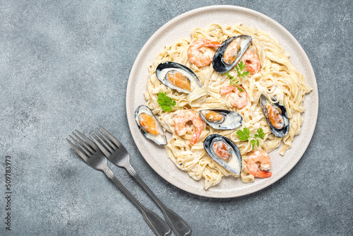 Pasta in a creamy sauce with seafood in a plate on a gray concrete background. Fettuccine with prawns and mussels. Top view, flat lay.