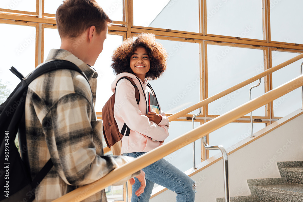 Two classmates climbing college stairs. Smiling woman student looking at her classmate on staircase. Two classmates climbing college stairs. Smiling woman student looking at her classmate on staircase.