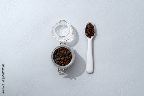 Glass jar with coffee beans and spoon on gray background